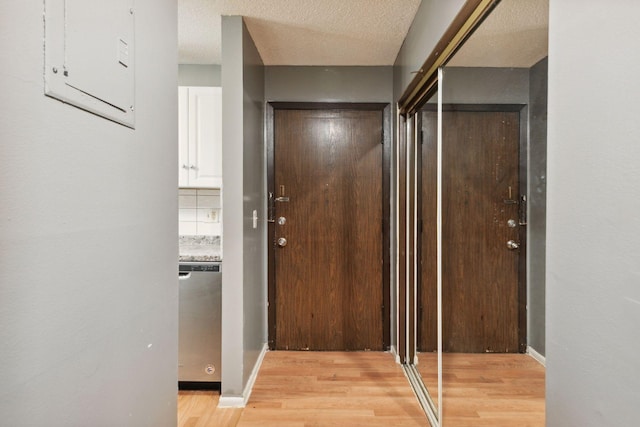 hallway with baseboards, light wood-type flooring, and a textured ceiling