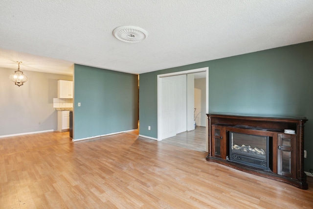 unfurnished living room featuring baseboards, a chandelier, a glass covered fireplace, and light wood-style floors