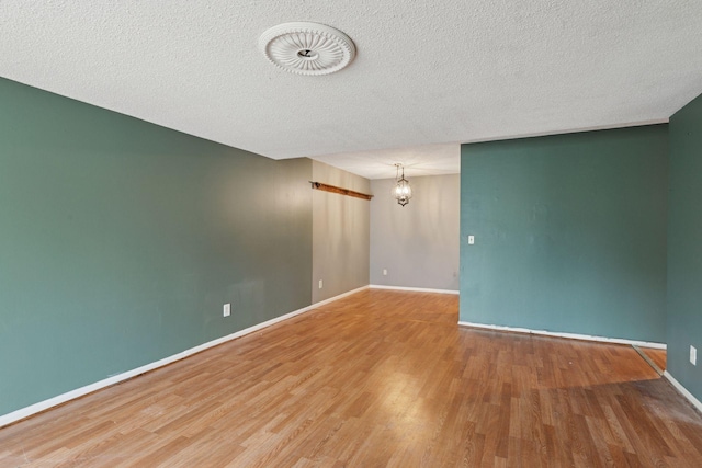 spare room with baseboards, a textured ceiling, wood finished floors, and a chandelier