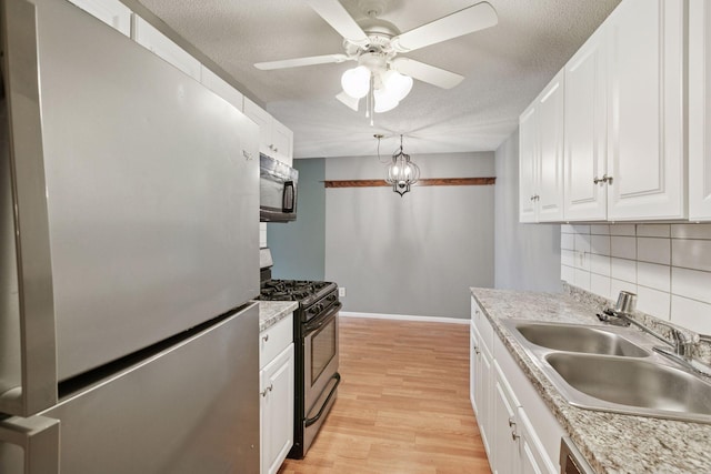 kitchen with a sink, light wood-style floors, stainless steel appliances, a ceiling fan, and backsplash