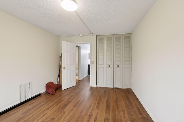 unfurnished bedroom featuring a textured ceiling, visible vents, wood finished floors, baseboards, and a closet