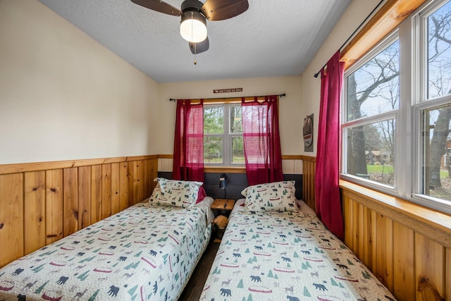 1171 County Rd E, Scott Twp, WI 54801 - bedroom featuring wooden walls, ceiling fan, wainscoting, and a textured ceiling