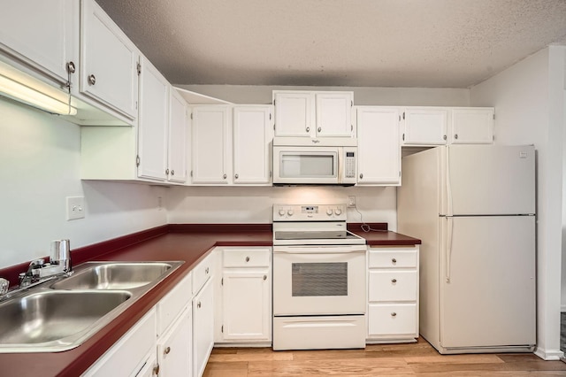 kitchen with dark countertops, light wood-type flooring, a sink, white cabinets, and white appliances