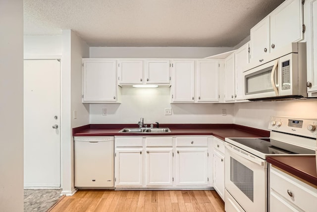 kitchen with white appliances, dark countertops, a sink, and white cabinets