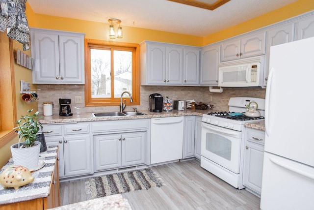 kitchen with tasteful backsplash, white appliances, light wood finished floors, and a sink