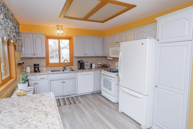 kitchen with white appliances, decorative backsplash, light wood-style flooring, and a sink