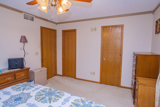 carpeted bedroom featuring ceiling fan, visible vents, baseboards, ornamental molding, and multiple closets