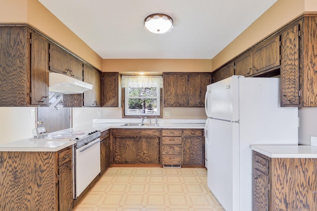 kitchen with a sink, light countertops, under cabinet range hood, light floors, and white appliances