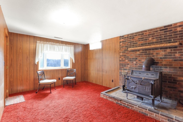 sitting room with a wood stove, wooden walls, and carpet floors
