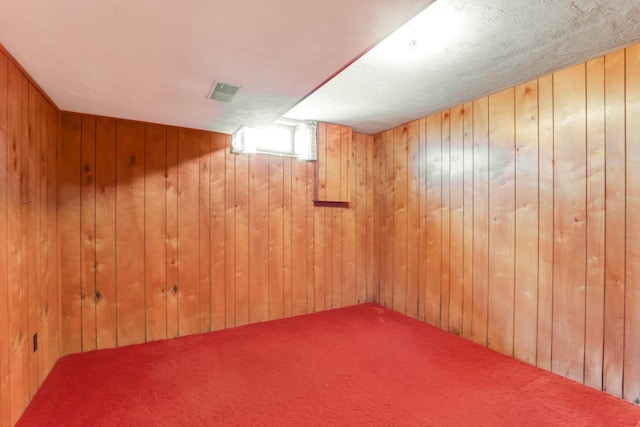 below grade area with wood walls, visible vents, and carpet flooring