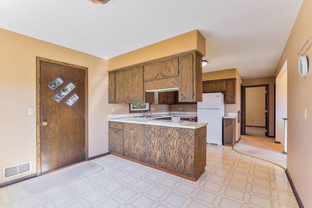 kitchen with visible vents, a peninsula, light countertops, freestanding refrigerator, and light floors