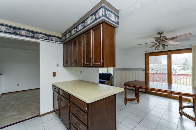 kitchen featuring ceiling fan, dark brown cabinets, light countertops, baseboards, and wallpapered walls