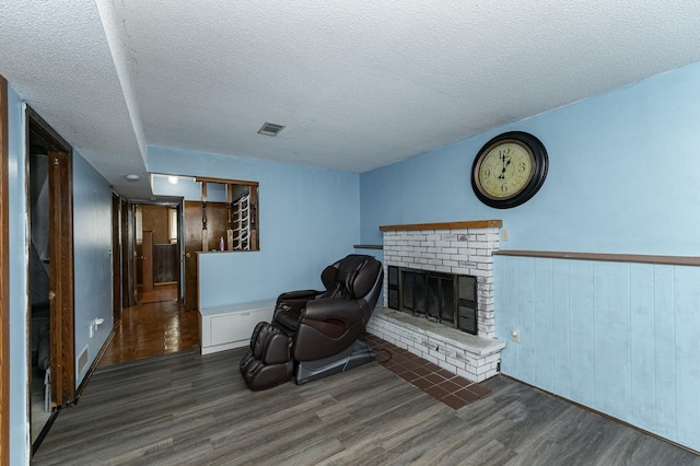 living area with visible vents, a textured ceiling, a brick fireplace, and wood finished floors