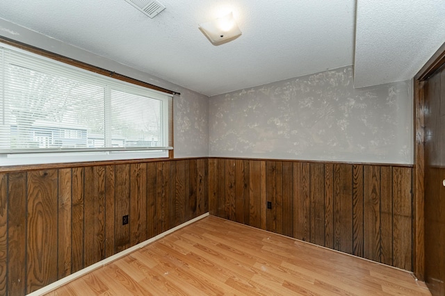 empty room featuring a textured ceiling, visible vents, a wainscoted wall, wooden walls, and light wood-style floors