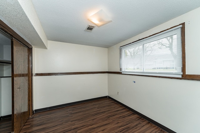 empty room with baseboards, dark wood-style floors, a textured ceiling, and visible vents