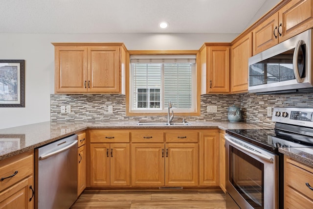 kitchen with a sink, light wood-style flooring, light stone countertops, and stainless steel appliances