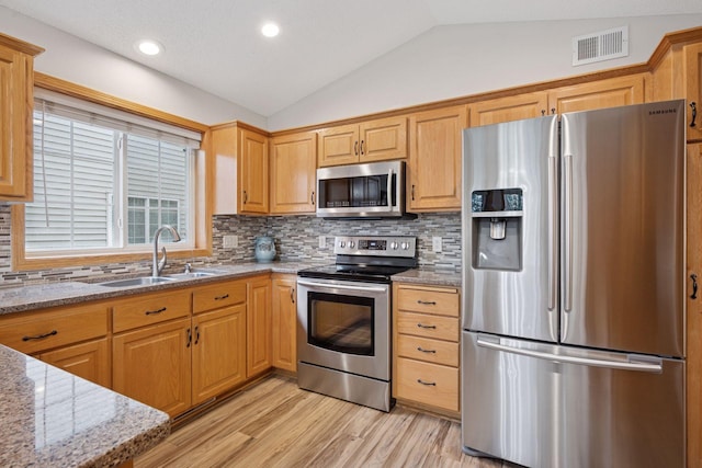 kitchen with appliances with stainless steel finishes, a sink, visible vents, light wood-style flooring, and vaulted ceiling