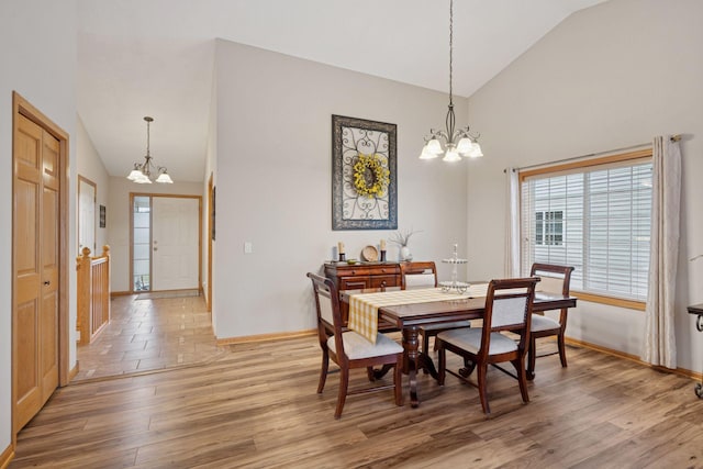 dining area featuring baseboards, light wood-type flooring, high vaulted ceiling, and a chandelier