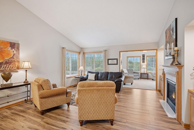 living room with a glass covered fireplace, baseboards, high vaulted ceiling, and light wood-style flooring