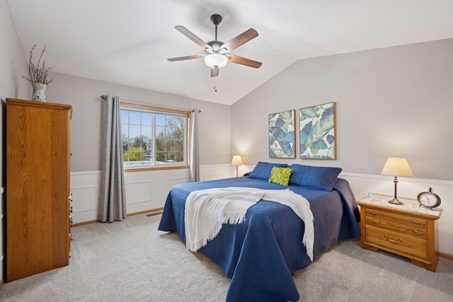 carpeted bedroom with a wainscoted wall, a ceiling fan, and vaulted ceiling