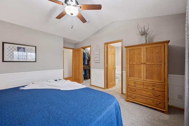 bedroom featuring a closet, wainscoting, light carpet, a walk in closet, and vaulted ceiling