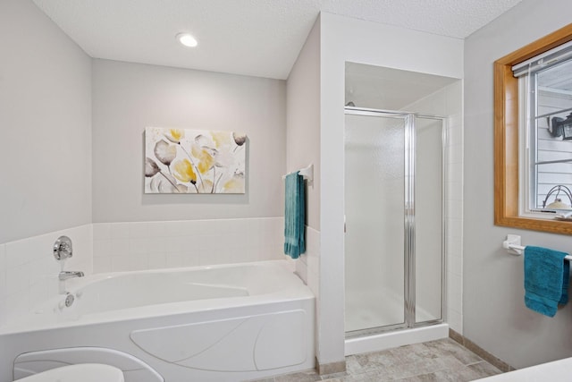 bathroom featuring a textured ceiling, baseboards, a shower stall, and a garden tub