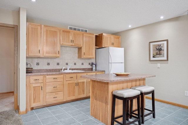 kitchen with freestanding refrigerator, visible vents, a sink, and light brown cabinets
