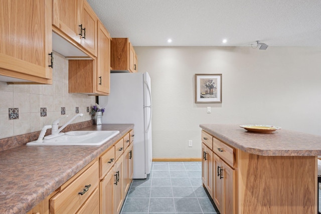 kitchen featuring a kitchen island, tasteful backsplash, a sink, baseboards, and freestanding refrigerator