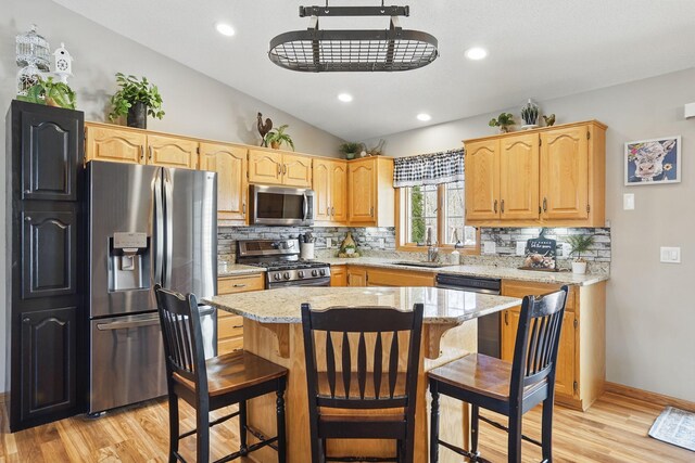 kitchen with a sink, light wood finished floors, stainless steel appliances, lofted ceiling, and tasteful backsplash