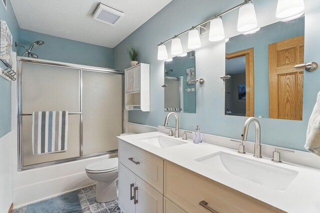 bathroom with double vanity, a sink, toilet, and shower / bath combination with glass door