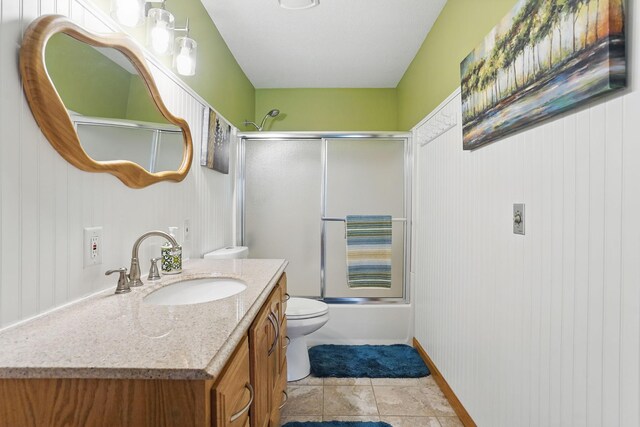 bathroom with toilet, bath / shower combo with glass door, tile patterned flooring, and vanity