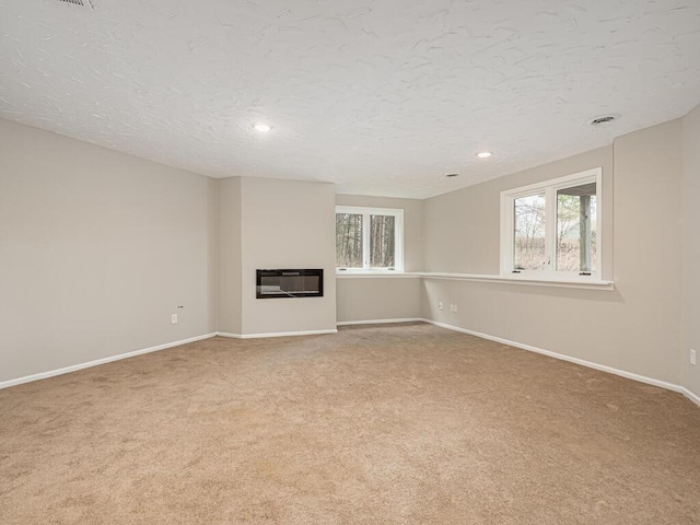 unfurnished living room featuring heating unit, a textured ceiling, carpet flooring, and a glass covered fireplace