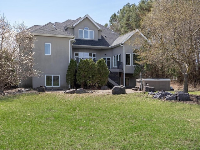 back of property featuring a yard, a shingled roof, stucco siding, and a hot tub