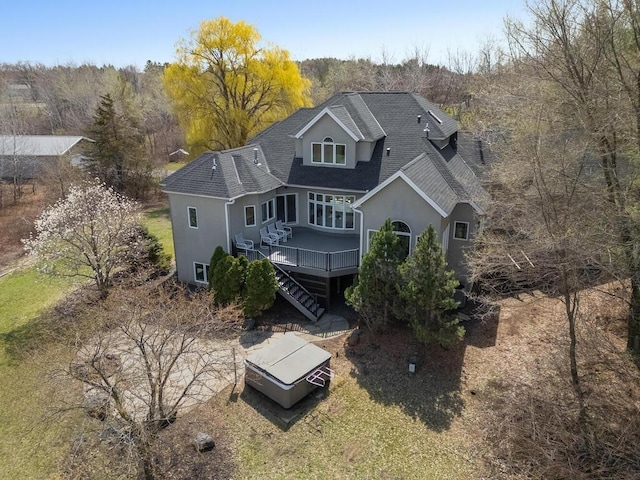 rear view of property featuring stairway, a shingled roof, a deck, stucco siding, and a wooded view