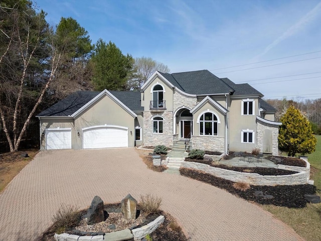 traditional-style home featuring stucco siding, decorative driveway, stone siding, roof with shingles, and an attached garage