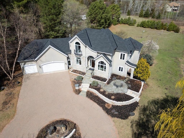 view of front of home featuring a front lawn, stucco siding, stone siding, decorative driveway, and an attached garage