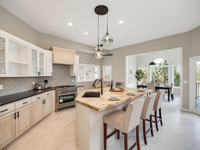 kitchen with light tile patterned floors, decorative backsplash, stainless steel range, and a sink