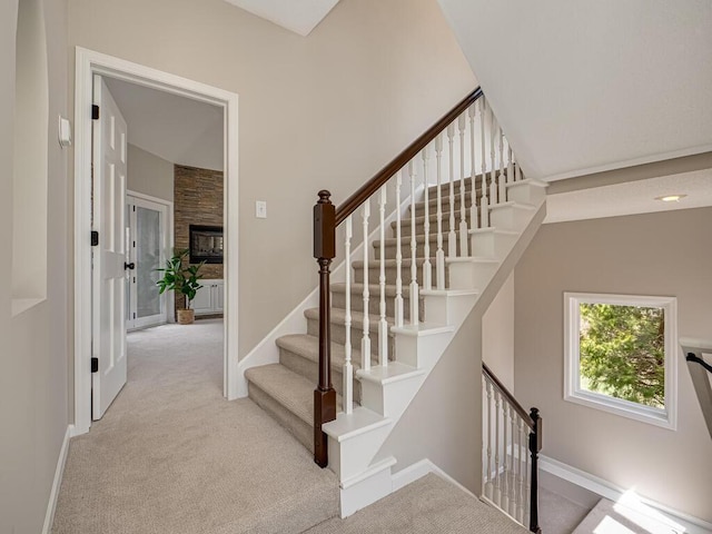 staircase with a stone fireplace, carpet, and baseboards
