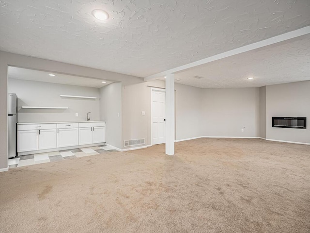 unfurnished living room with a textured ceiling, visible vents, light colored carpet, and baseboards