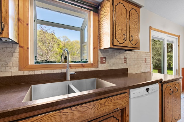7830 Country Ln, Lino Lakes, MN 55014 - kitchen with white dishwasher, a sink, dark countertops, brown cabinetry, and backsplash