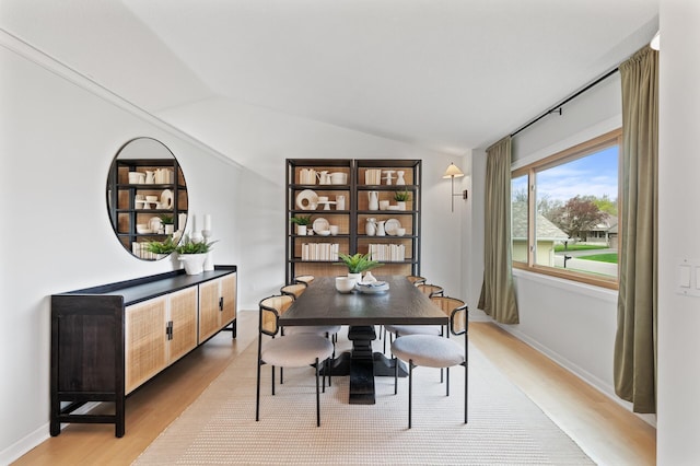 dining space featuring baseboards, light wood-type flooring, and vaulted ceiling