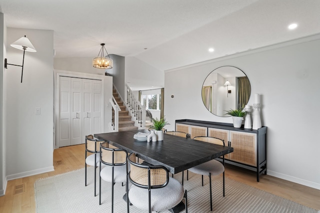 dining room with light wood finished floors, vaulted ceiling, visible vents, and stairs