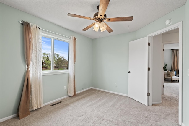 carpeted empty room featuring a textured ceiling, visible vents, baseboards, and a ceiling fan