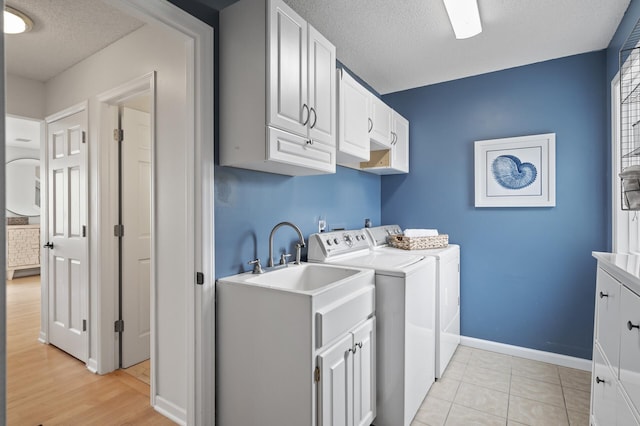 clothes washing area with a textured ceiling, baseboards, light tile patterned floors, washing machine and clothes dryer, and cabinet space