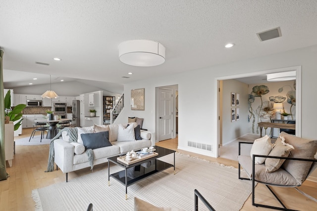 living area with stairs, light wood-style floors, visible vents, and vaulted ceiling