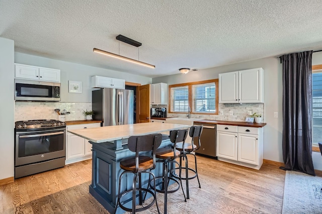 8 Queen Ave S, Minneapolis, MN 55405 - kitchen with stainless steel appliances, a textured ceiling, white cabinets, backsplash, and a breakfast bar area