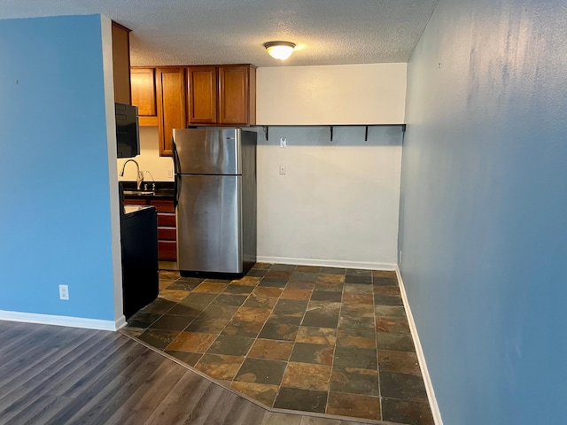 kitchen featuring freestanding refrigerator, brown cabinets, baseboards, a textured ceiling, and dark countertops