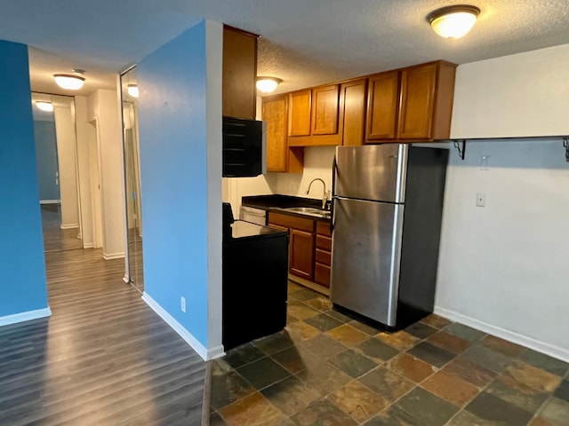 kitchen with freestanding refrigerator, a sink, dark countertops, baseboards, and brown cabinetry