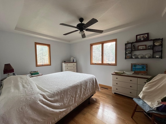 14879 Benson Rd, Grantsburg, WI 54840 - bedroom featuring baseboards, multiple windows, a tray ceiling, and wood finished floors