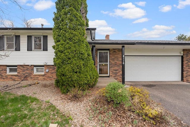 view of front of house featuring a garage, a chimney, brick siding, and aphalt driveway